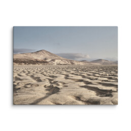 Un vasto paisaje desértico con onduladas dunas de arena se extiende hacia las lejanas montañas bajo un cielo azul claro, que recuerda al impresionante Lienzo Sotavento. Una escasa vegetación se aferra a la base de estos majestuosos picos.