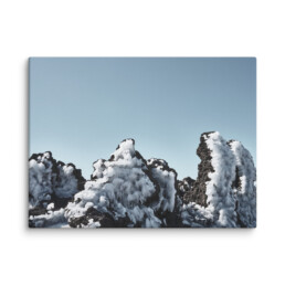 Un paisaje rocoso con picos nevados bajo un cielo azul claro que recuerda al Lienzo Roque helado. Las rocas oscuras resaltan contra la nieve blanca y brillante, creando una escena natural impactante.