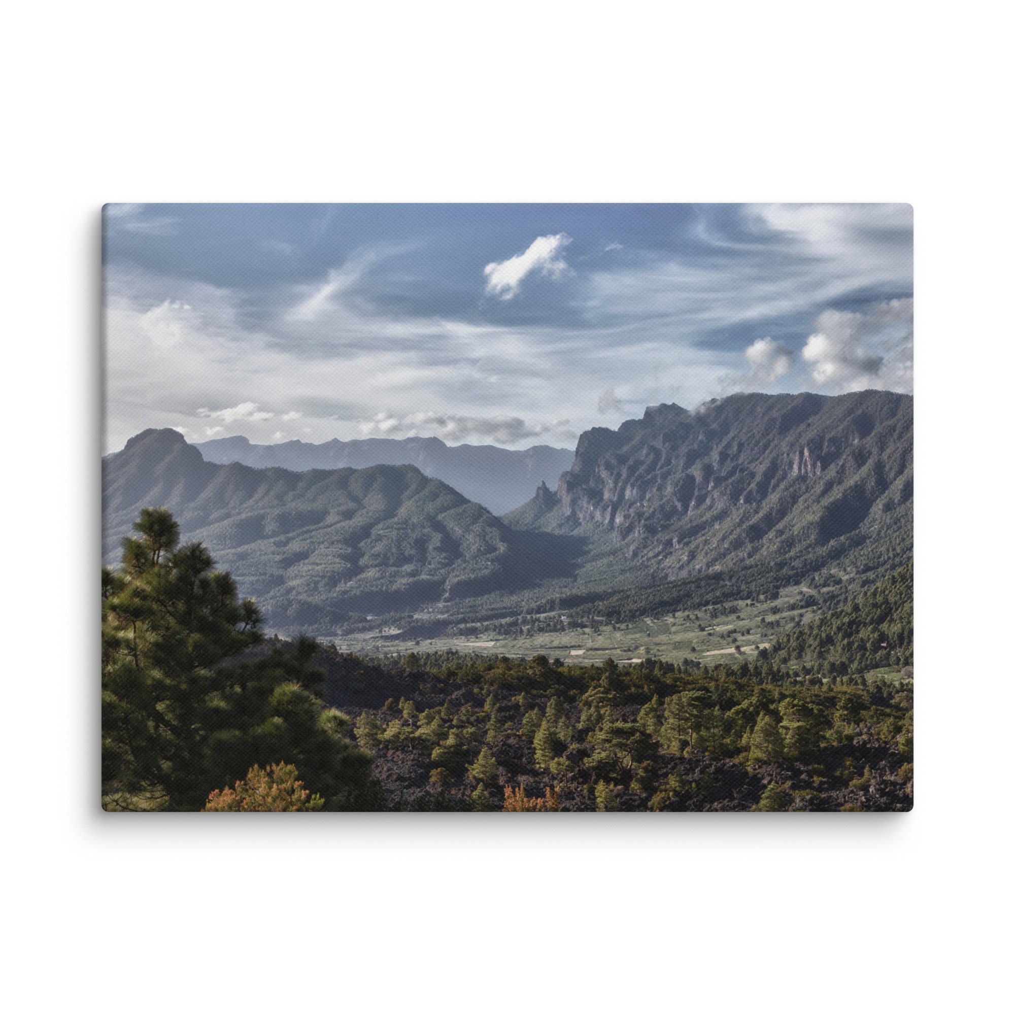 Un paisaje espectacular con montañas verdes y exuberantes bajo un cielo nublado. En primer plano, los pinos y el terreno rocoso crean un contraste con la vista expansiva de colinas boscosas y picos distantes, evocando el estilo del Lienzo Caldera de Taburiente de Volcanica Productions.