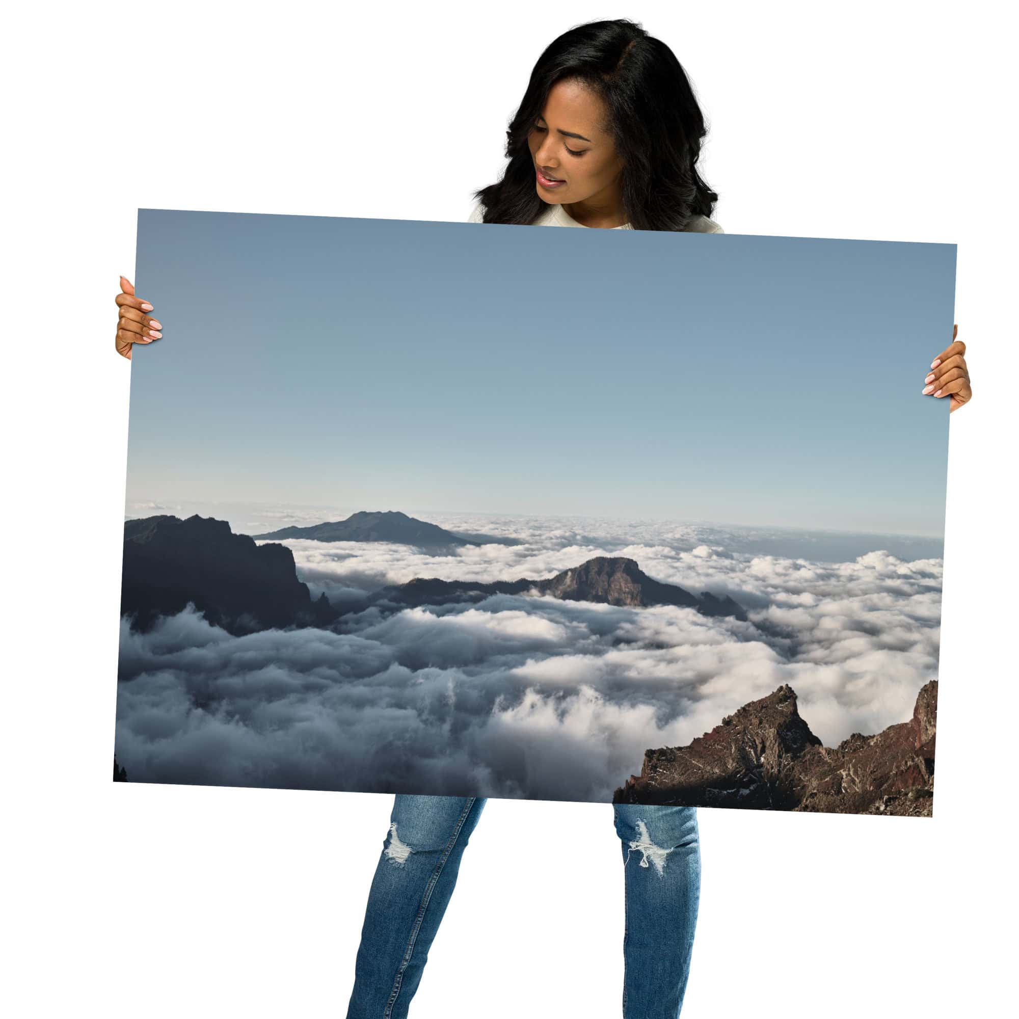 Una persona con una camiseta negra y unos vaqueros sostiene nuestro cartel "Mar de nubes desde el Roque de los Muchachos", que muestra una impresionante vista panorámica de las montañas y las nubes de La Palma. El fondo blanco liso complementa a la perfección esta exquisita pieza de arte decorativo, lo que la hace ideal para añadirla a tu carrito en nuestra tienda online.