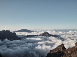 El Póster mar de nubes desde el Roque de los Muchachos captura un impresionante paisaje montañoso, donde escarpados picos se elevan a través de un mar de nubes blancas bajo un cielo azul claro, encarnando la dramática belleza típica del Arte Decorativo y reflejando la esencia tranquila de los Paisajes Canarios.