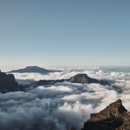 El Póster mar de nubes desde el Roque de los Muchachos captura un impresionante paisaje montañoso, donde escarpados picos se elevan a través de un mar de nubes blancas bajo un cielo azul claro, encarnando la dramática belleza típica del Arte Decorativo y reflejando la esencia tranquila de los Paisajes Canarios.