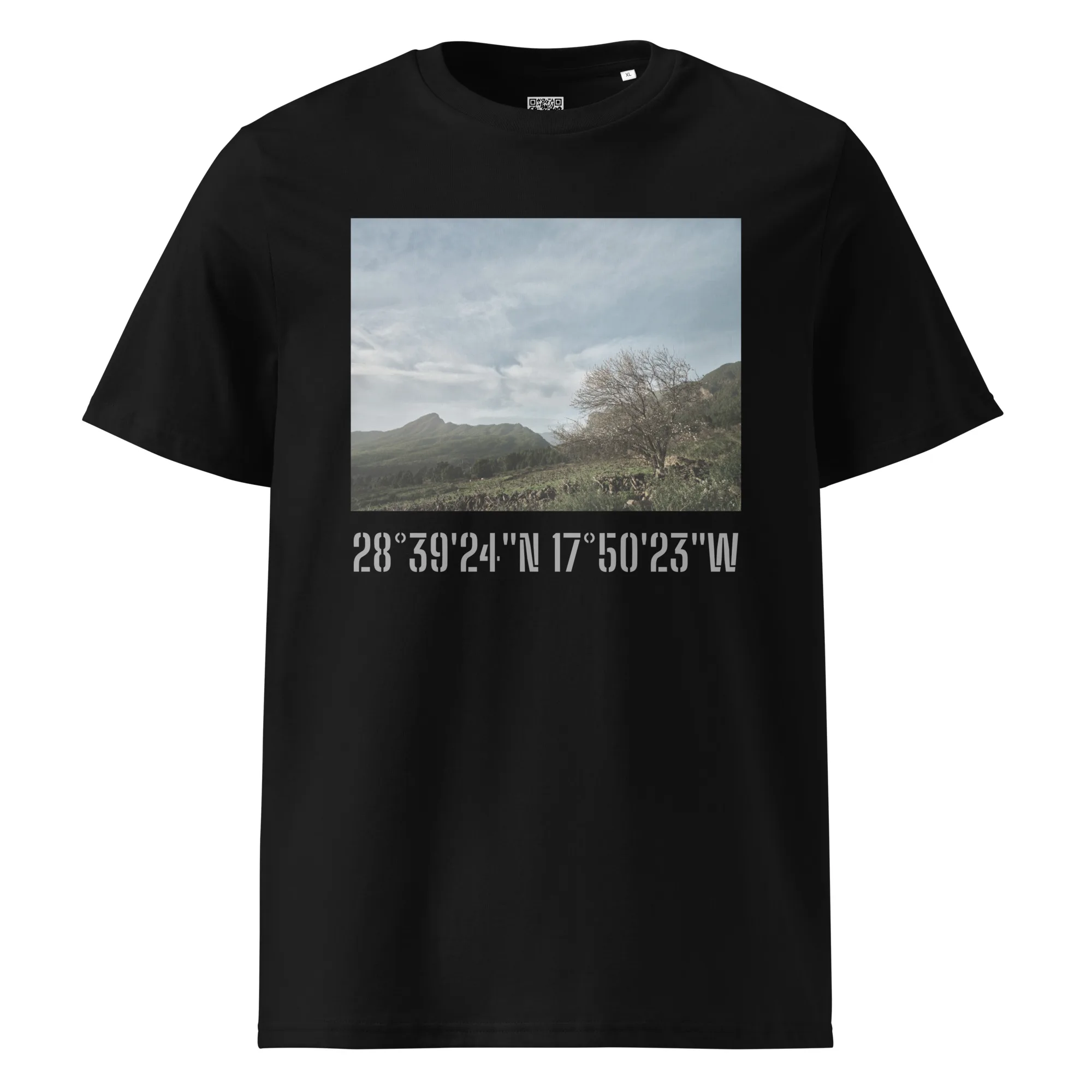 La camiseta unisex negra "Camiseta Unisex Camino Virgen del Pino", que muestra una imagen de un paisaje de montañas y árboles bajo un cielo nublado, resume la esencia de Paisajes Canarios en La Palma. Debajo de la imagen, encontrarás las coordenadas: 28°3924N 17°5023W.