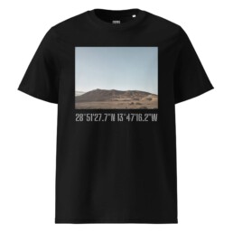 Impresionante camiseta unisex de Los Ajaches en color negro, que muestra un cautivador paisaje desértico con dunas de arena y una montaña bajo un cielo azul claro. Debajo de esta pintoresca escena se encuentran las coordenadas geográficas: 28°5127.7N 13°4716.2W, que recuerdan las impresionantes vistas de La Palma.