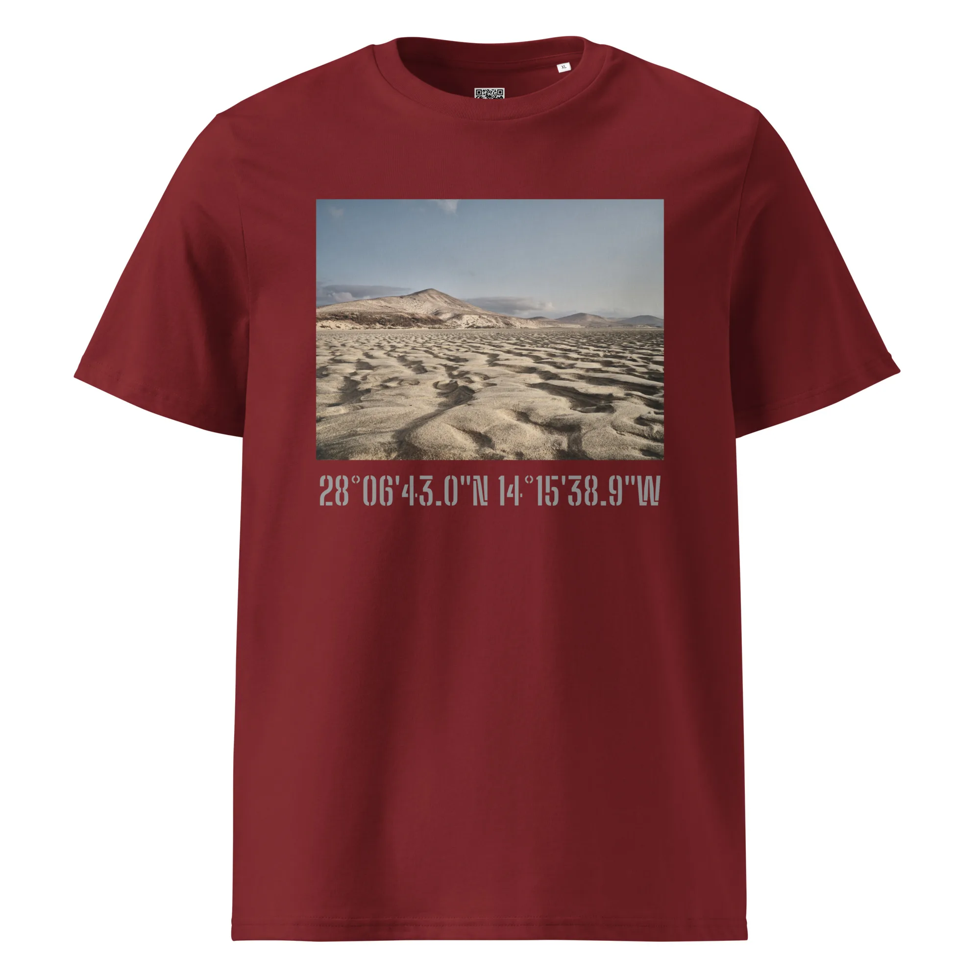 La camiseta unisex Sotavento presenta un cautivador paisaje desértico con escarpadas dunas de arena bajo un cielo nublado en color granate. Debajo de la imagen, las coordenadas geográficas se muestran elegantemente en texto blanco, lo que le da un toque de Arte Decorativo que recuerda a Paisajes Canarios.