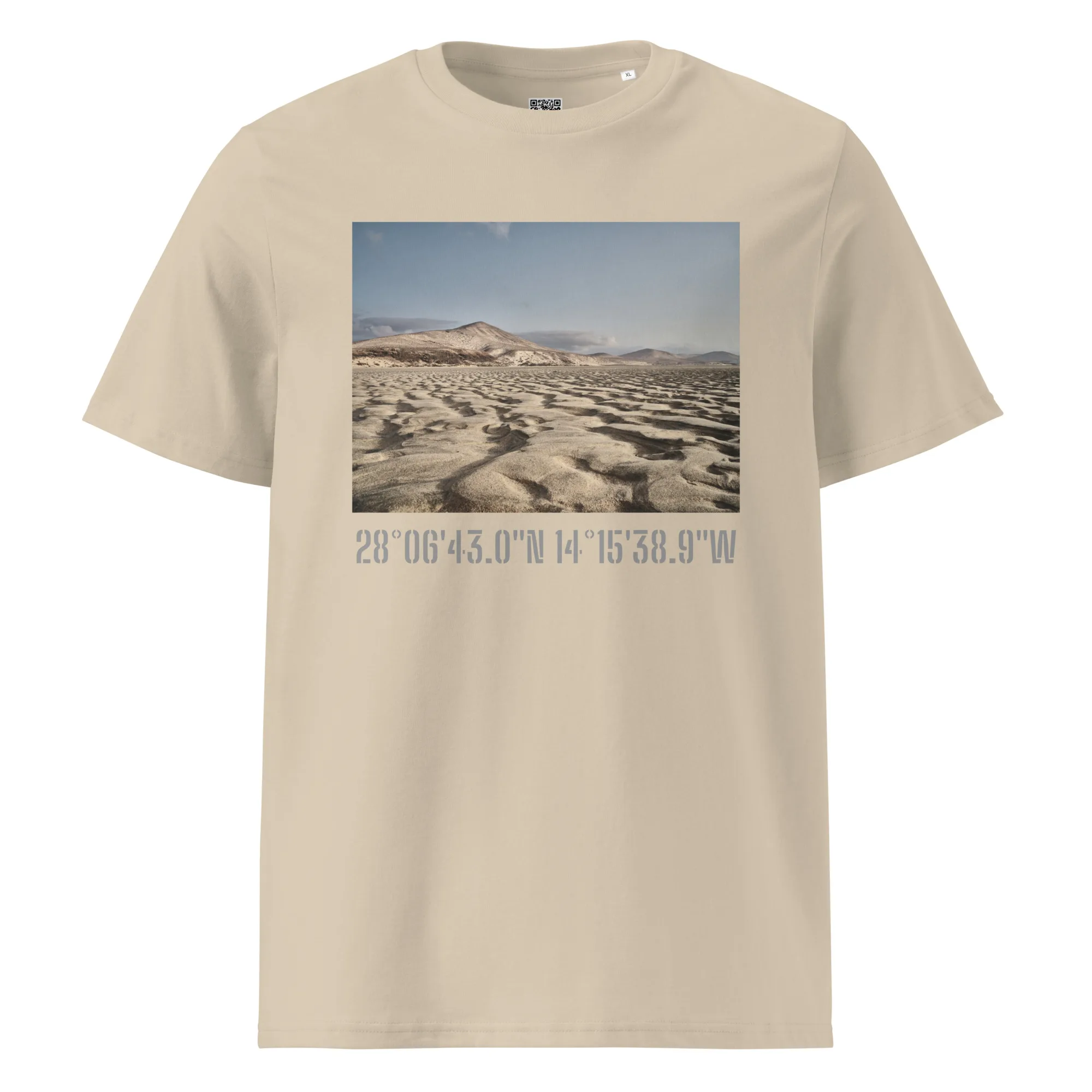 La Camiseta unisex Sotavento de Tienda Online presenta un diseño en color beige con una fotografía de un paisaje desértico con montañas lejanas bajo un cielo despejado, capturando la esencia de Paisajes Canarios. Debajo de esta impresionante imagen se encuentran impresas las coordenadas: 28°0643.0N 14°1538.9W.