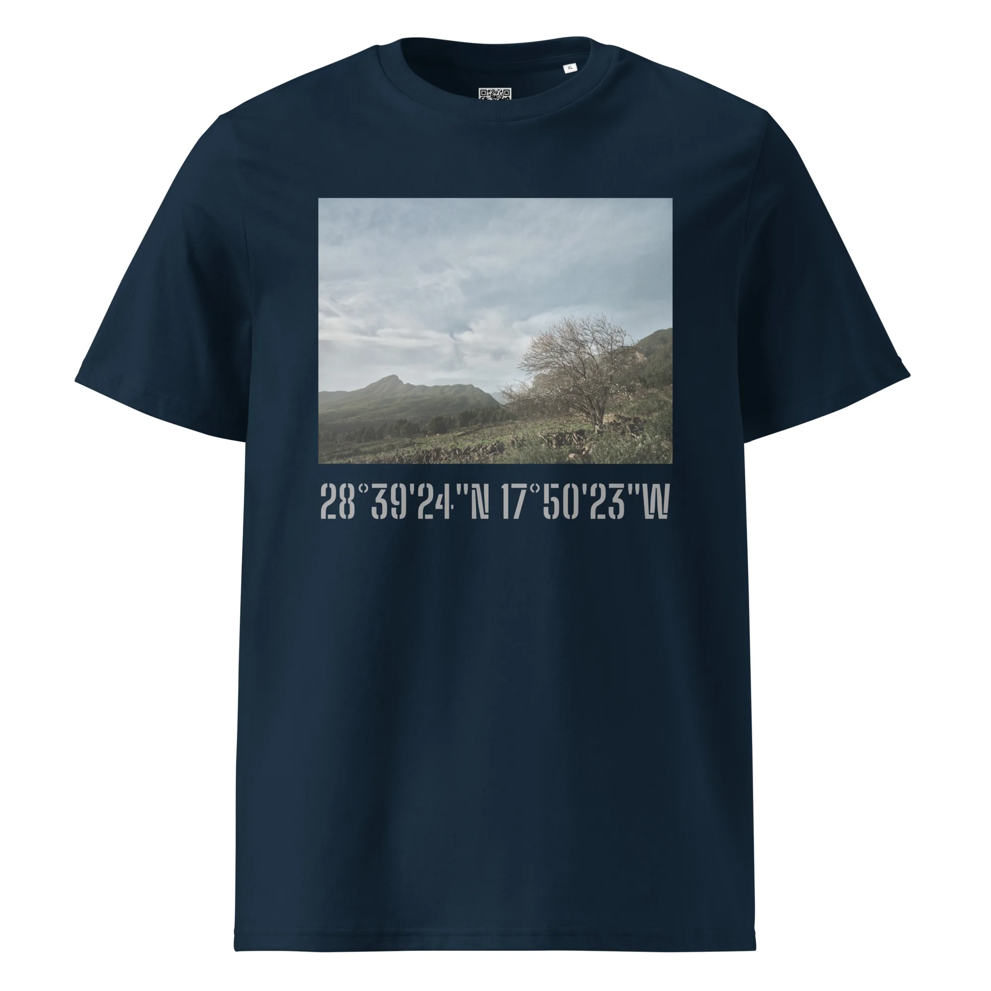 La camiseta unisex Camino Virgen del Pino de color negro presenta un paisaje escénico que representa las montañas y los árboles de La Palma bajo un cielo nublado. Las coordenadas geográficas 28°3924N 17°5023W están impresas debajo de la imagen, lo que resalta su ubicación exótica. Disponible para comprar en Tienda Online de Volcanica Productions.