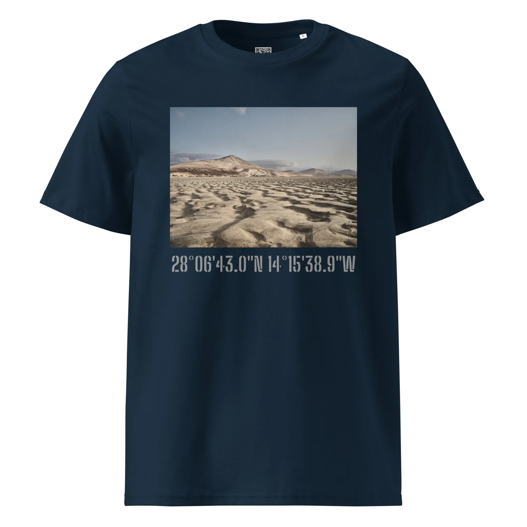 Esta camiseta unisex Sotavento de Volcanica Productions presenta un impresionante paisaje desértico con dunas de arena bajo un cielo azul claro. Debajo de la imagen vibrante, el texto blanco muestra las coordenadas: 28°0643.0N 14°1538.9W, disponible ahora en nuestra Tienda Online.